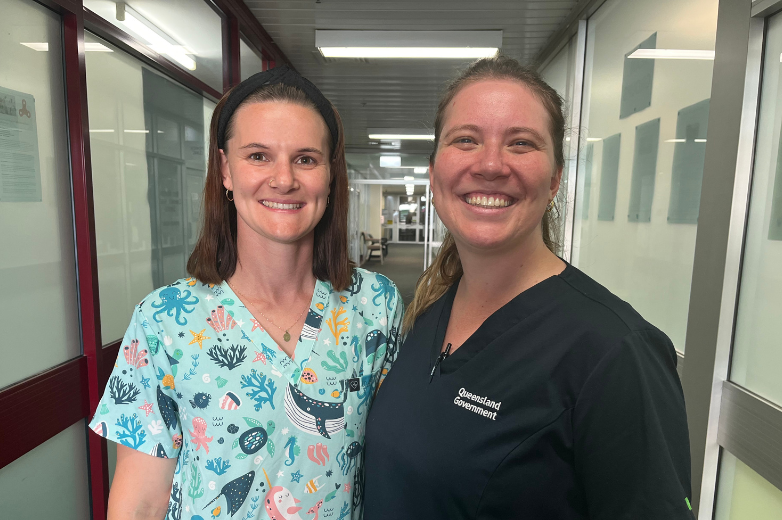 Two women wearing nursing scrubs standing in a hallway smiling